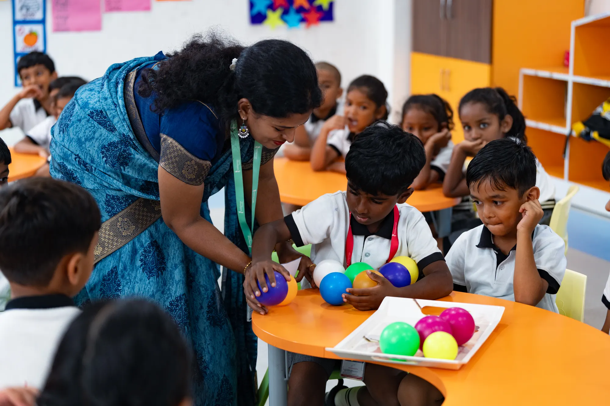 A Wellsprings teacher leaning over a table to help a student sort colourful balls