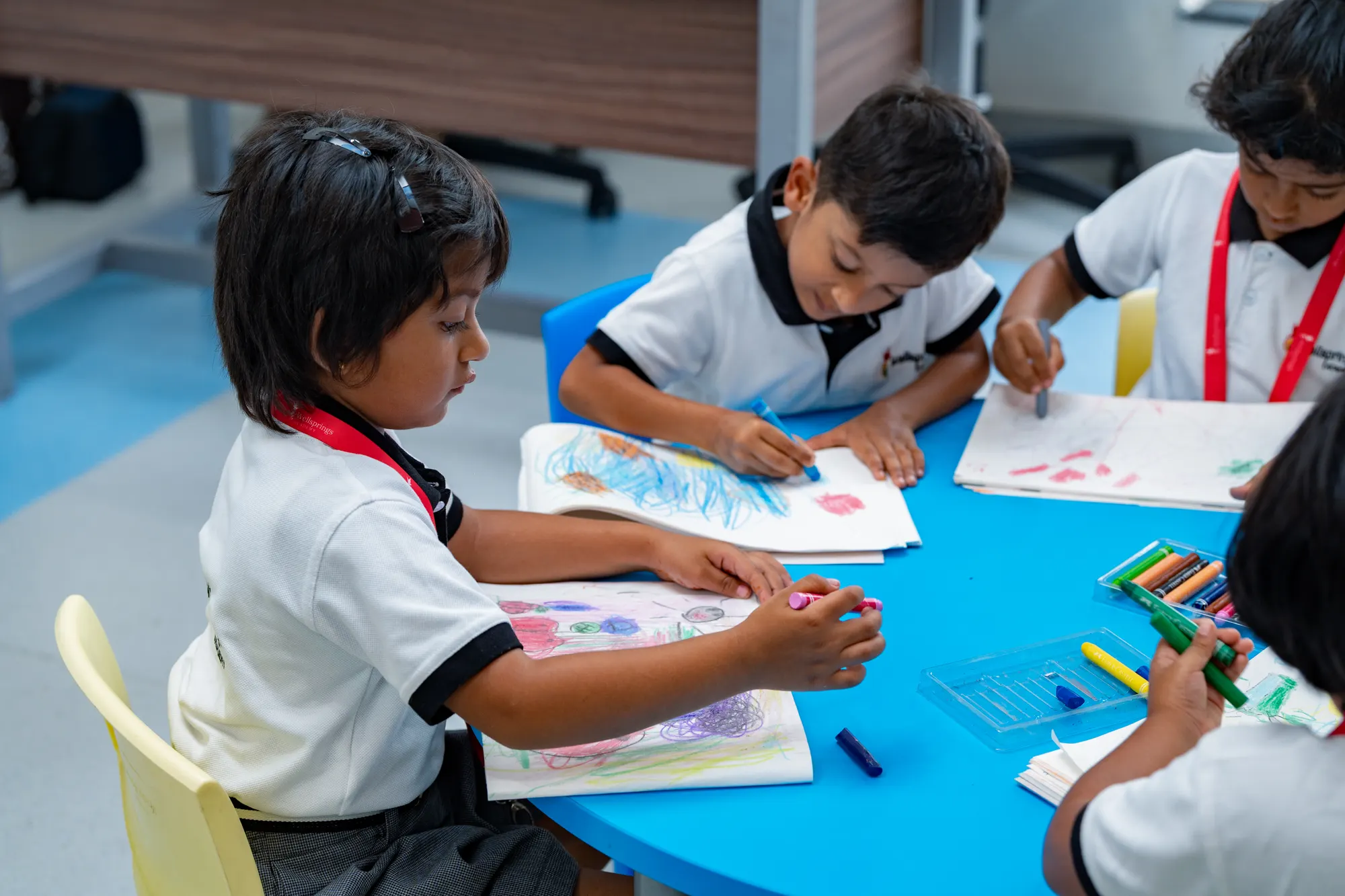 Young Wellsprings students drawing with crayons