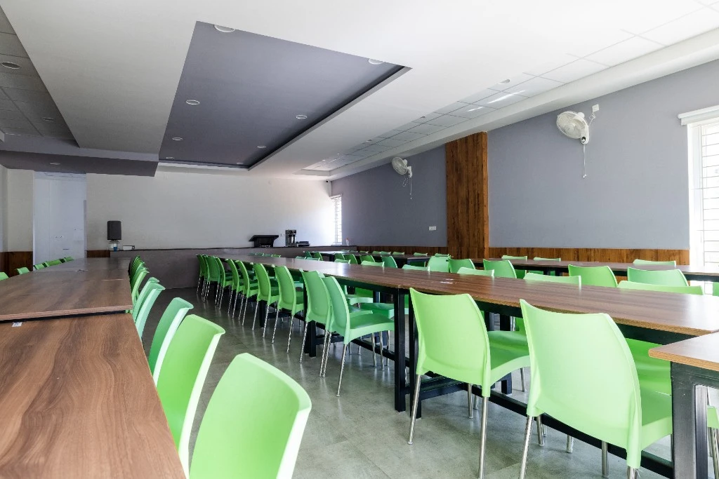 The cafeteria with long tables and green chairs