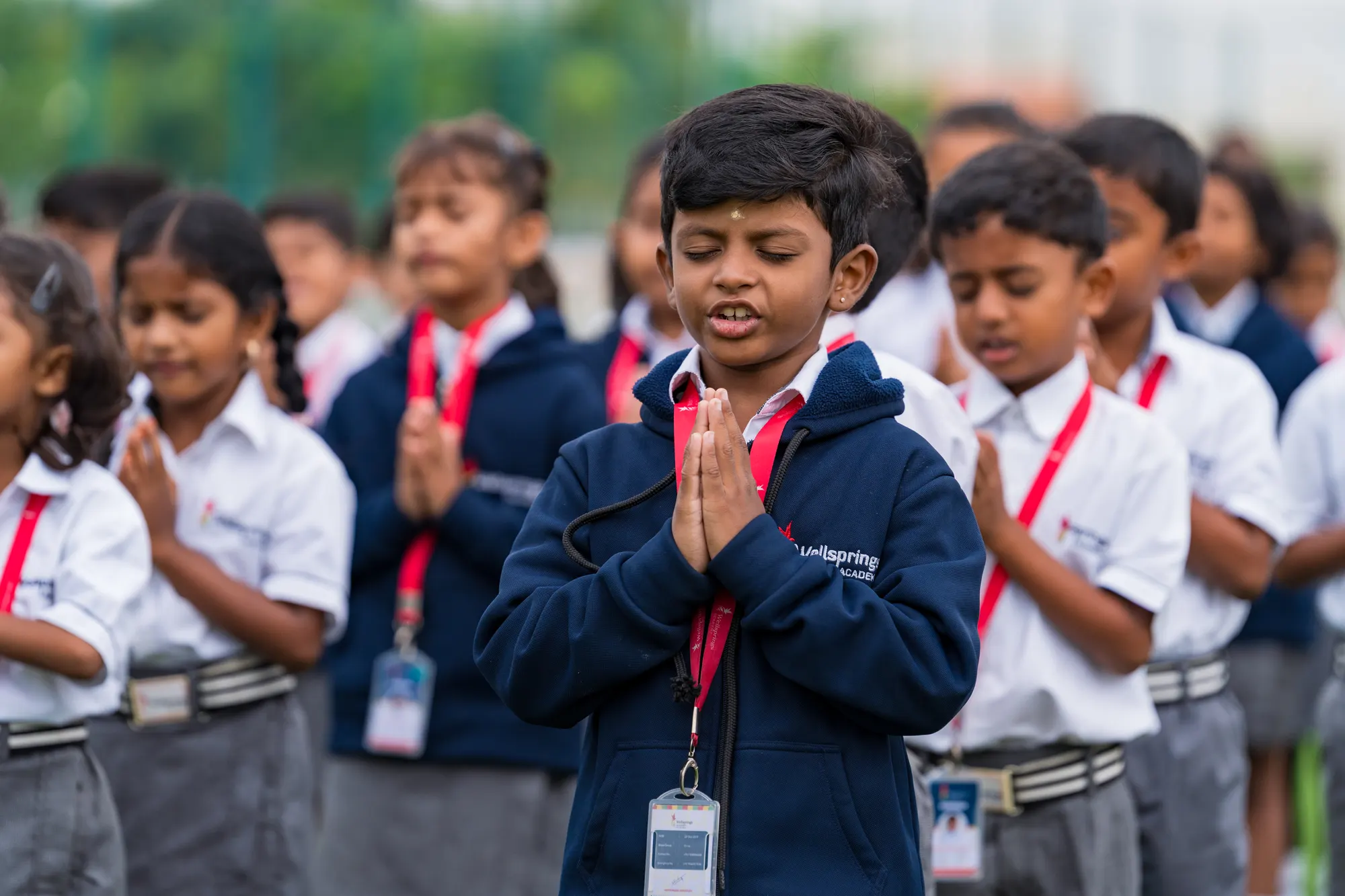 A Wellsprings student standing with his hands together during assembly